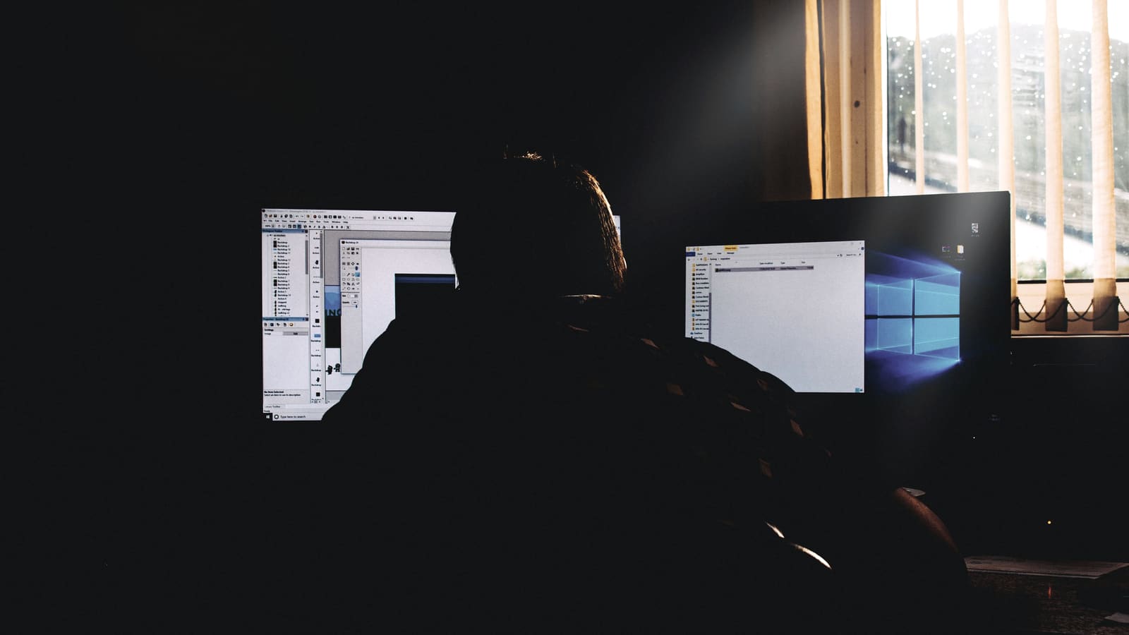 Postazione di lavoro con due schermi accesi in un ufficio in penombra